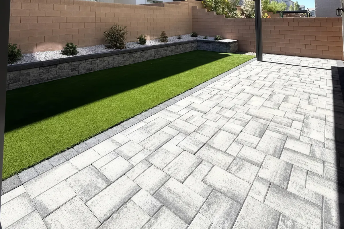 Covered paver patio with a turf lawn and planter wall in a Las Vegas backyard