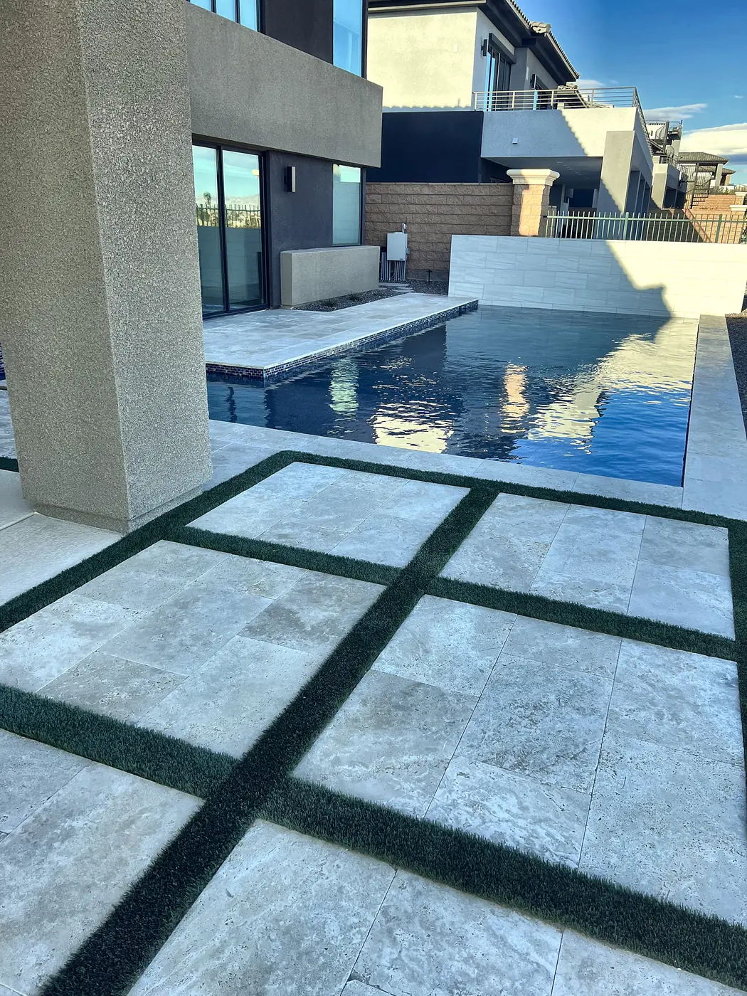 Travertine and turf at the pool edge, a Unique Pavers job in the Las Vegas valley