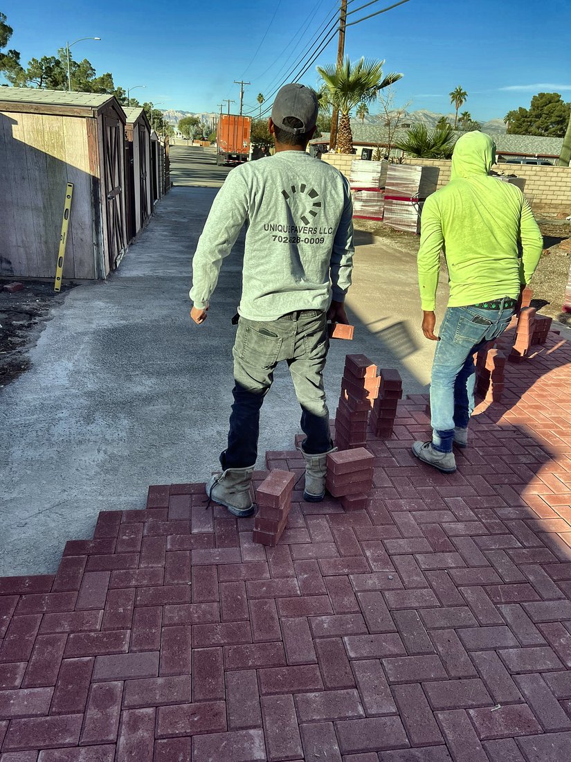 Two Unique Pavers crew members carrying pavers across a new red herringbone driveway