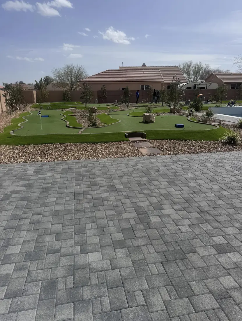 Backyard putting green with a gray paver patio, boulders, and a pool at a Las Vegas home